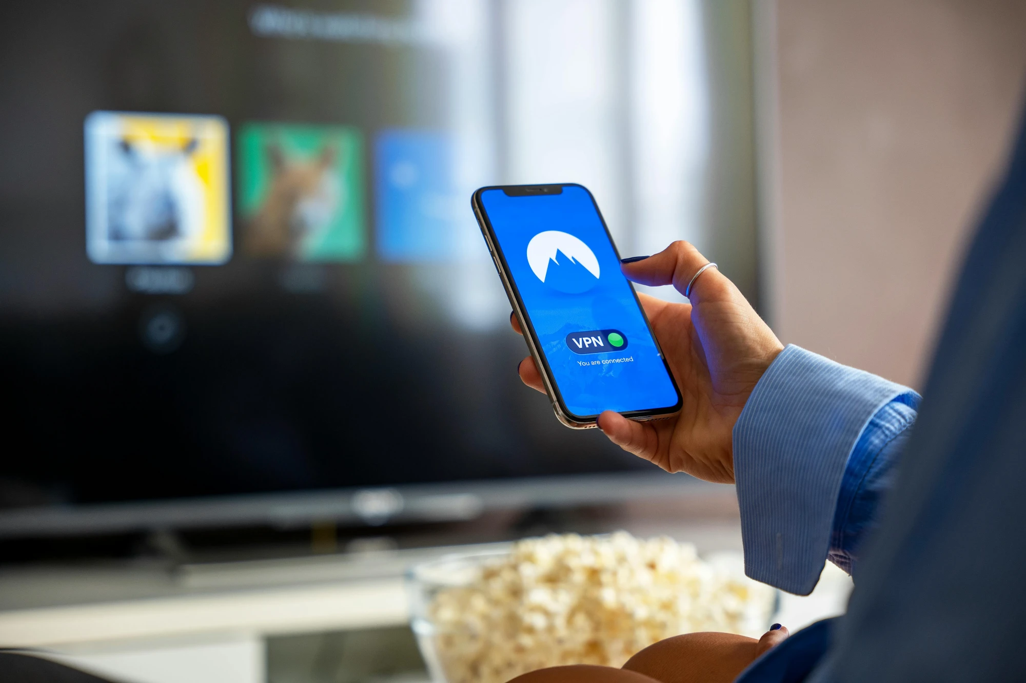 Hand houdt een smartphone vast voor een televisiescherm