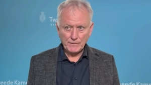 Jan Struijs voor een wand met het logo van de Tweede Kamer